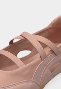 Chaussure rose à bout fermé avec des lanières élastiques croisées et des détails cousus sur le côté, conçue pour un usage décontracté.