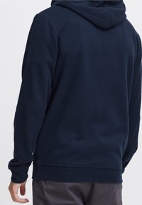 Sudadera azul marino hecha de tela suave, con un bolsillo tipo canguro, puños acanalados y capucha con cordón. Textura suave, ajuste relajado.