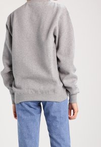 Sweat-shirt gris avec un design simple, poignets et ourlet côtelés, associé à un jean bleu clair. Le tissu semble doux et texturé.