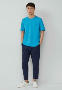 Blauwe katoenen T-shirt met een borstzak, gecombineerd met marineblauwe taps toelopende broek en witte sneakers. Eenvoudig ontwerp met een ronde hals.