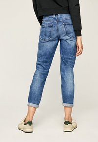 Blue denim jeans with a tapered fit, cuffed hem, and two back pockets. Features a light wash and subtle texture.