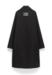 Cappotto lungo nero con colletto, dotato di una patch rettangolare sul retro. Texture liscia, design oversize e senza chiusure visibili.