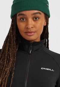 Sort fleecetrøje med lynlås og høj krave, med hvidt "O'NEILL" logo. Accessorieseret med en grøn ribstrikket beanie. Teksturstof.