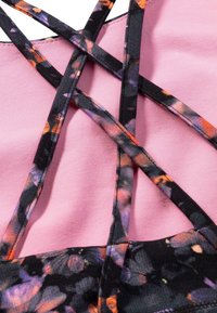 Floral-patterned fabric in black, purple, and orange intersected by black straps on a pink background, featuring smooth texture and crisscross design.