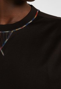 Svart t-shirt med rund hals som har flerfärgad sömnad längs halsringningen och en mjuk bomullstextur.