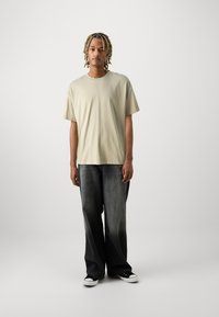 Lichtbeige T-shirt met korte mouwen, ontspannen pasvorm, gecombineerd met donker vervaagde wijde jeans en zwarte sneakers met witte zolen.