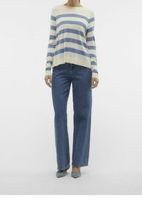 Pull à manches longues rayé crème et bleu, associé à un jean bleu taille haute à jambes larges. Caractéristiques : texture douce et coupe décontractée.