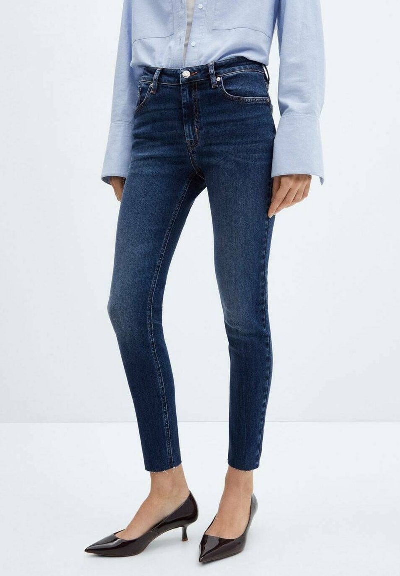 Jean skinny bleu foncé en denim, avec une taille mi-haute, cinq poches et un design classique. Associé à des escarpins à bout pointu.