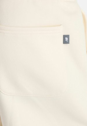 Tessuto color crema con una tasca quadrata cucita che presenta un piccolo etichetta nera con un logo bianco sul bordo destro.