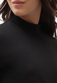 Musta korkeakauluksinen paita, joka on valmistettu pehmeästä ja sileästä kankaasta. Suunnittelussa on istuva siluetti, jossa on hillitty kiilto, eikä näkyviä kuvioita.