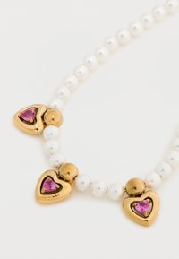 Χρυσά μενταγιόν σε σχήμα καρδιάς με ροζ πολύτιμους λίθους, εναλλάσσονται με λευκές μαργαριταρένιες χάντρες και χρυσά στρογγυλά διαχωριστικά σε σχέδιο κολιέ.