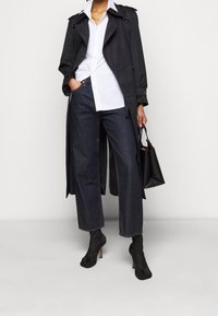 Czarny płaszcz trench z białą koszulą, zestawiony z szerokimi spodniami dżinsowymi w ciemnym kolorze i czarnymi botkami na obcasie. Uzupełniony czarną torebką.