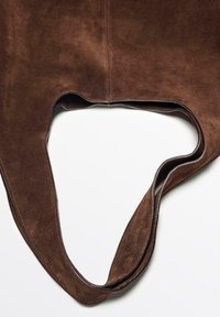Brązowa torebka z zamszu z wyciętym uchwytem. Miękka tekstura, bezszwowy design i wzmocnione krawędzie podkreślają nowoczesny styl torby.