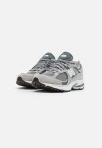 Gray athletic shoes featuring a mix of mesh and suede materials, with a white midsole and black rubber outsole. Notable 'N' logo on the side.