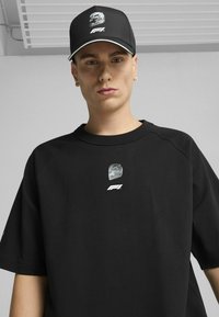 Must värvi oversized T-särk, millel on graafiline logo keskel, koos sobiva musta mütsi ja hõbedase aktsendi ning logoga.