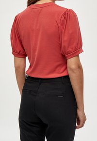 Červený žebrovaný top s krátkým rukávem a nabíranými rukávy; v kombinaci s černými kalhotami se bočními kapsami a slim fit.