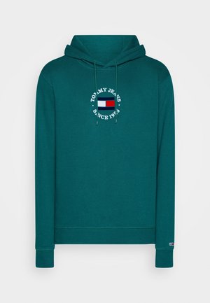Turquoise hoodie met een logo-applicatie aan de voorkant en witte tekst met de woorden "Tommy Jeans Since 1985", met een klein rood-wit-blauw vlagembleem.