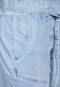 Pantalones cortos de mezclilla azul claro con un bolsillo frontal, costuras cosidas y cierre de botón. La tela tiene una textura suave y una apariencia desgastada.
