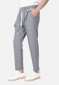 Pantaloni grigi a sigaretta con vita elasticizzata, due tasche laterali e cordoncino. Indossati con sneakers bianche. Tessuto liscio e leggero.