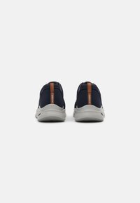 Zapatillas deportivas azul marino con parte superior de malla flexible, suela gris claro y una lengüeta naranja en el talón para facilitar el calzado.