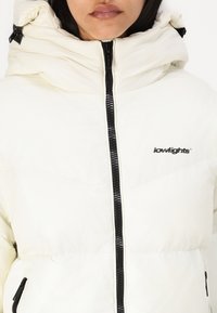 White puffer jacket with a high collar, front zipper, and black accents. Features a logo and quilted texture for insulation.