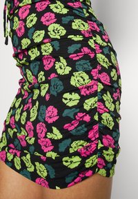 Schwarzes Kleid mit leuchtend pink und grünem Blumendruck, mit gerafften Seiten und einer figurbetonten Silhouette.