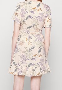 Kukallinen kietaisumekko pehmeästä beige-kankaan, jossa on violetteja, vihreitä ja ruskeita kuvioita. Ominaisuudet lyhyet hihat ja röyhelöhelma.