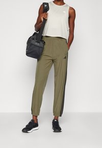 Jasnoszary krótki top na ramiączkach z małym logo, oliwkowozielone zwężane spodnie z czarnymi bocznymi paskami oraz czarne buty sportowe. W zestawie czarna torba na ramię.