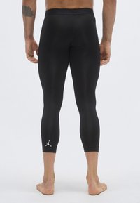 Μαύροι συμπιεστικοί κολάν με ε φαρμοστή γραμμή, με λευκό λογότυπο κοντά στο τελείωμα και λεία, ελαστική υφή. Χωρίς ορατές ραφές.