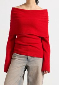 Rød off-the-shoulder sweater lavet af blødt stof med lange ærmer og et lagdelt design. Kombinationen med lyseblå jeans.