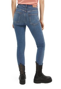 Jeans skinny de denim azul con una cintura alta y dos bolsillos traseros, combinados con botas negras hasta el tobillo con cremalleras laterales.