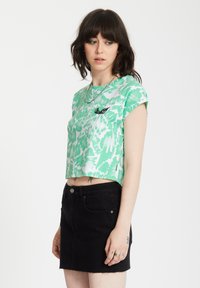 Groene cropped tie-dye shirt met opgerolde mouwen en een zwart geborduurd logo, gecombineerd met een zwarte spijkerrok met een rafelrand.