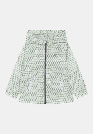 Veste de pluie blanche à capuche avec motif d'ancre verte, fermeture éclair sur le devant et poches latérales.