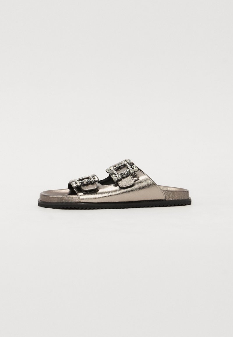 Sandales à glissière argentées métalliques avec deux boucles ornées, design ouvert à l'avant et semelle noire texturée. Surface lisse avec des accents minimaux.
