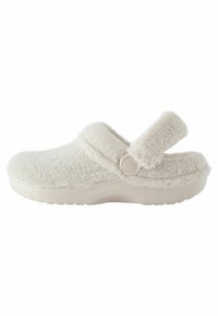 Sabots blancs et confortables en matériau doux et duveteux, dotés d'une bride à boucle ronde et d'une semelle robuste et texturée pour une bonne adhérence et un confort optimal.