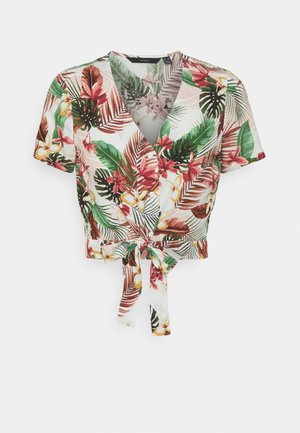 Blouse courte à manches courtes avec imprimé floral tropical, col en V, boutons sur le devant et nouée à la taille sur un fond blanc.
