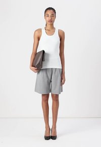 Weißes Top, graue maßgeschneiderte Shorts, schwarze High Heels und eine braune Clutch. Glattes Material und strukturierter Schnitt.