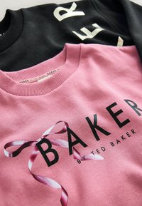 Felpe nere e rosa sovrapposte; la nera ha lettere bianche, mentre la rosa presenta un design a nastro con "BAKER by TED BAKER" in bold nero.