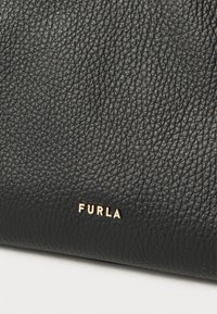 Μαύρη δερμάτινη τσάντα χειρός με υφή στην επιφάνεια και ανάγλυφο λογότυπο σε χρυσό χρώμα. Διαθέτει κομψό, σύγχρονο σχέδιο και μινιμαλιστικές λεπτομέρειες.