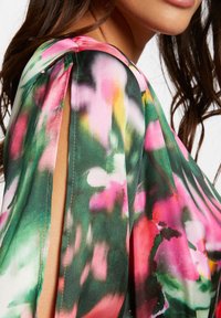 Blusa fluida in tessuto leggero con un motivo floreale nei toni del verde, rosa e giallo; presenta fessure sulle spalle per un tocco di stile.