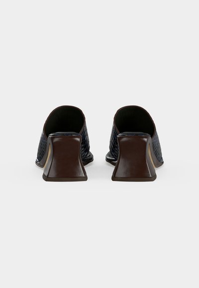 Ζευγάρι γαλάζιας-μπλε υφασμάτινα δερμάτινα mule παπούτσια με ανοιχτή φτέρνα, φαρδιά, χαμηλά καφέ μπλοκ τακούνια, εμφανιζόμενα από πίσω σε λευκό φόντο.