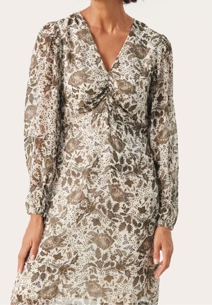 Kobieta w sukience z długim rękawem i dekoltem w serek, z marszczeniem z przodu oraz misternym brązowym kwiatowym wzorem na białym tle.