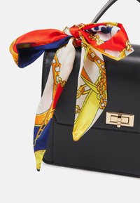 Sac à main en cuir noir avec un fermoir rectangulaire doré, orné d'un foulard en soie multicolore présentant des motifs de chaînes et géométriques attaché à la poignée.