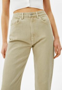 Ljusbeige vida jeansbyxor i denim, med framfickor, knäppning med knapp och stickad detalj längs sömmarna.