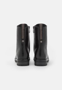 Par de botas negras de cuero hasta el tobillo con tacones apilados y tiradores de tela, vistas desde atrás sobre un fondo blanco.