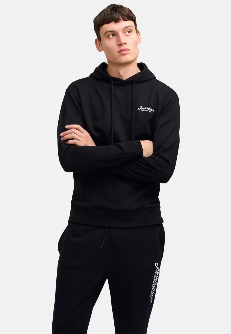Black hoodie with adjustable drawstring, front pocket, and logo on the chest. Paired with black sweatpants featuring logo detail on the side.