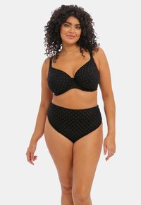 Černá souprava spodního prádla, která zahrnuje vzorované podprsenky s kosticemi a kalhotky vysokého pasu. Měkká tkanina s geometrickou texturou a nastavitelné ramínka.