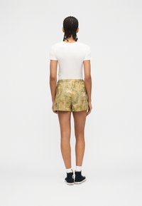 Personne avec des cheveux tressés portant un haut blanc à manches courtes, un short vert à motifs, des chaussettes blanches et des baskets montantes noires, vue de dos.