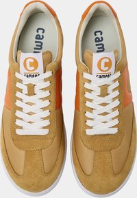 Zapatillas en tonos marrón y naranja con un acabado de ante texturizado y cuero suave. Presentan cordones blancos y una etiqueta con el logo en la lengüeta.