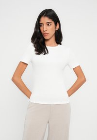 White fitted t-shirt made of ribbed material with short sleeves and a round neckline, paired with light beige wide-leg trousers.
